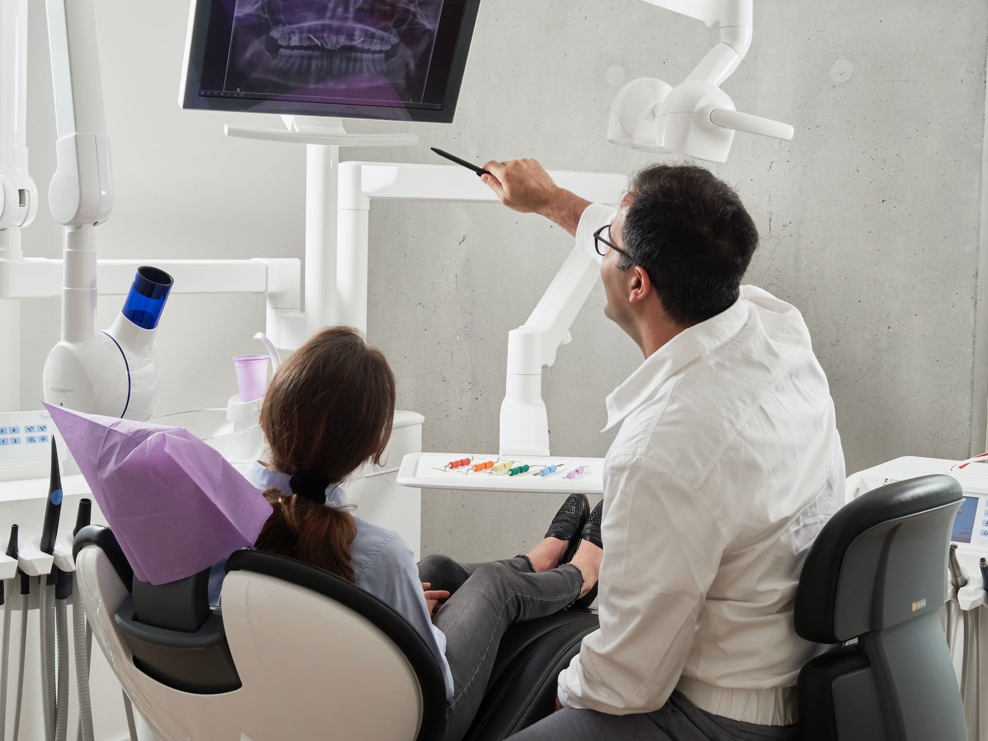 A dentist explaining a dental X-ray to a patient, pointing to areas of interest on the X-ray image.